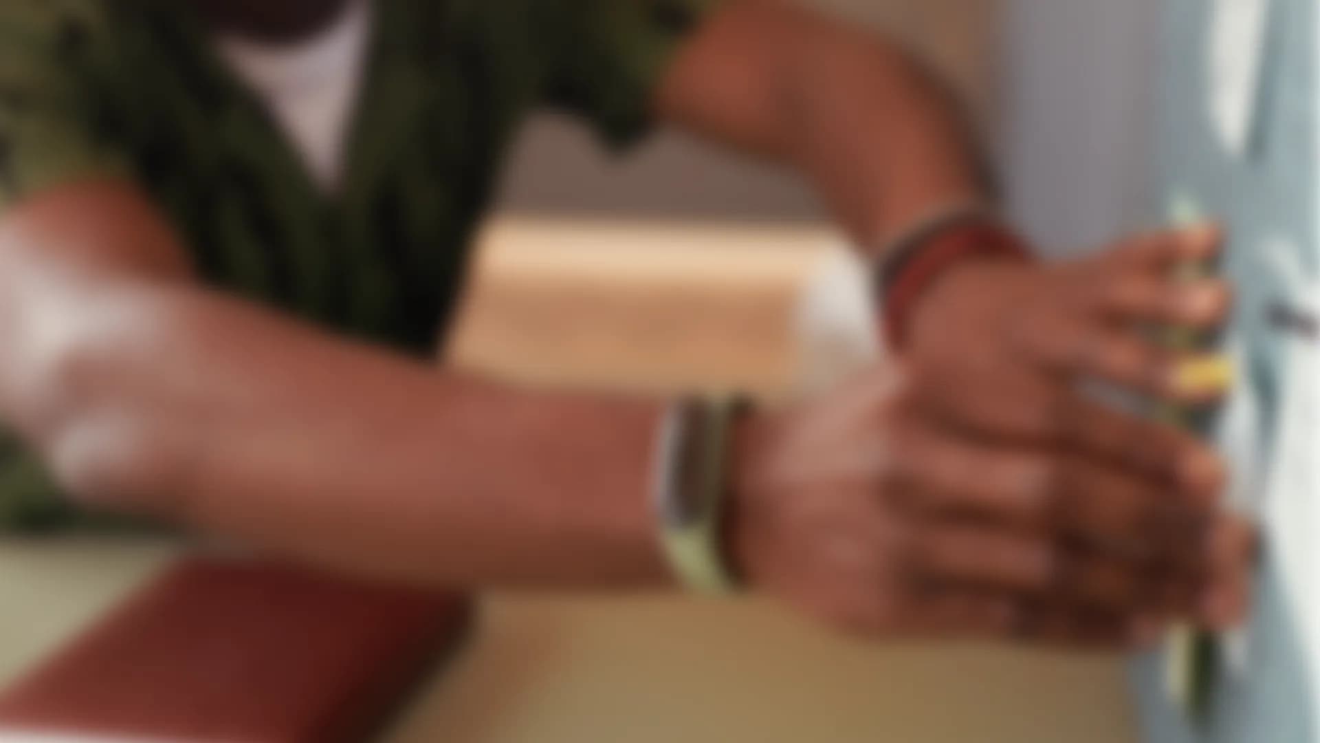 Two hands resting on a desk beside a notebook, out of focus