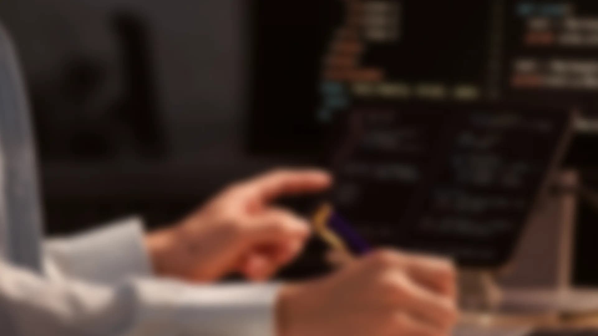 Hands at a laptop showing a dark dashboard, out of focus