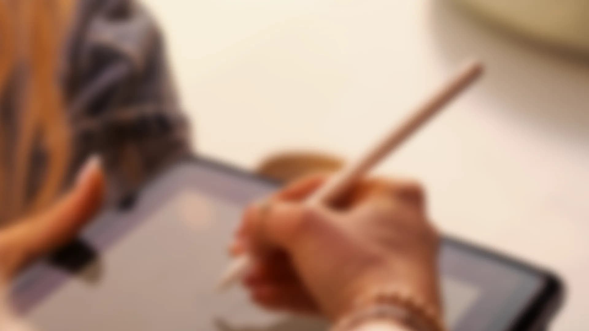 A hand writing on a tablet with a stylus, out of focus